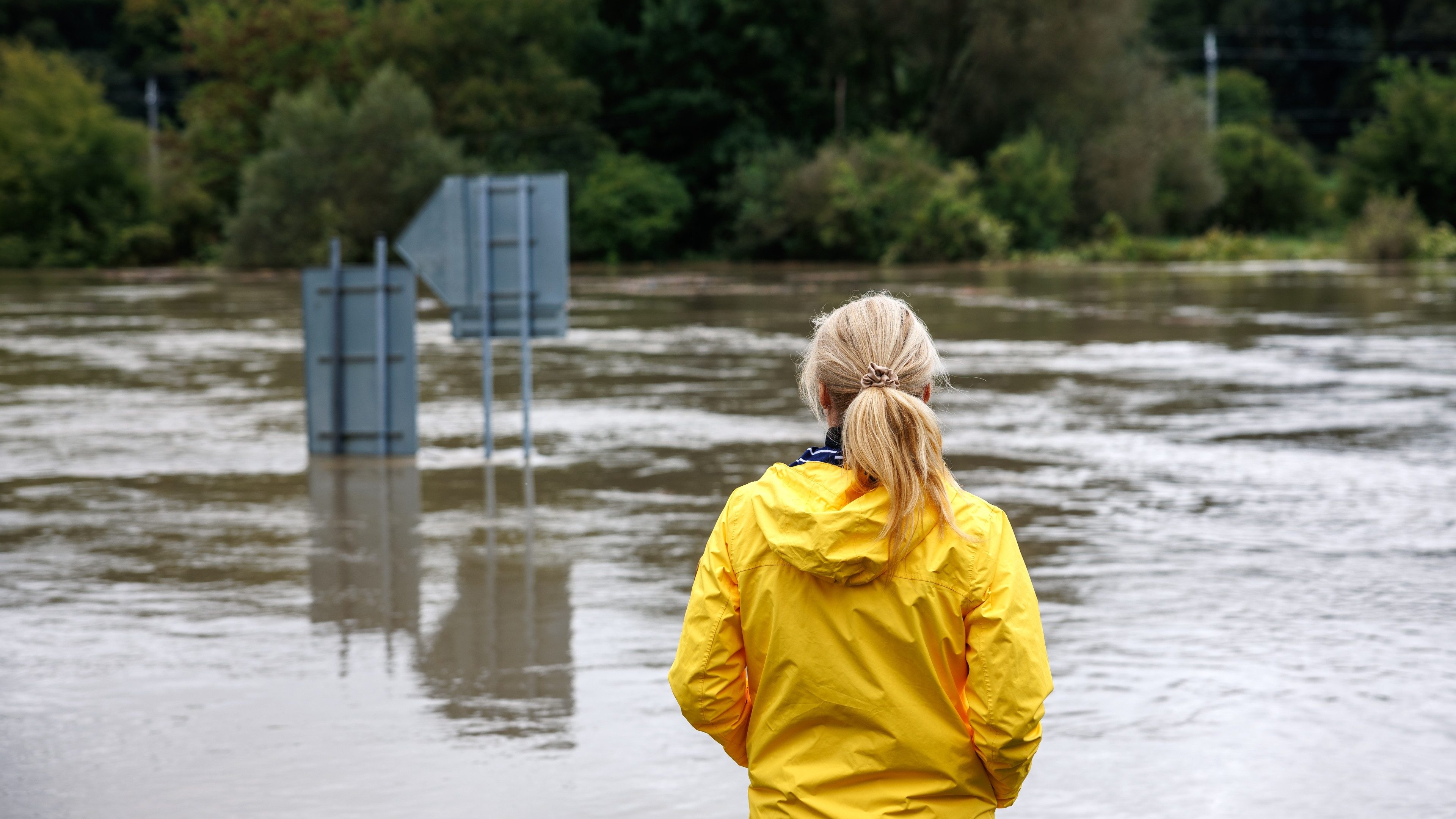 Flooded river. Worried woman looking at overflowing water during flood. Extreme weather and natural disaster